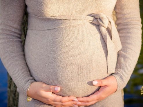 Clare Minter Therapies - Is Maternity Reflexology Safe? image of pregnant lady wearing a beige dressing holding her bump with her hands